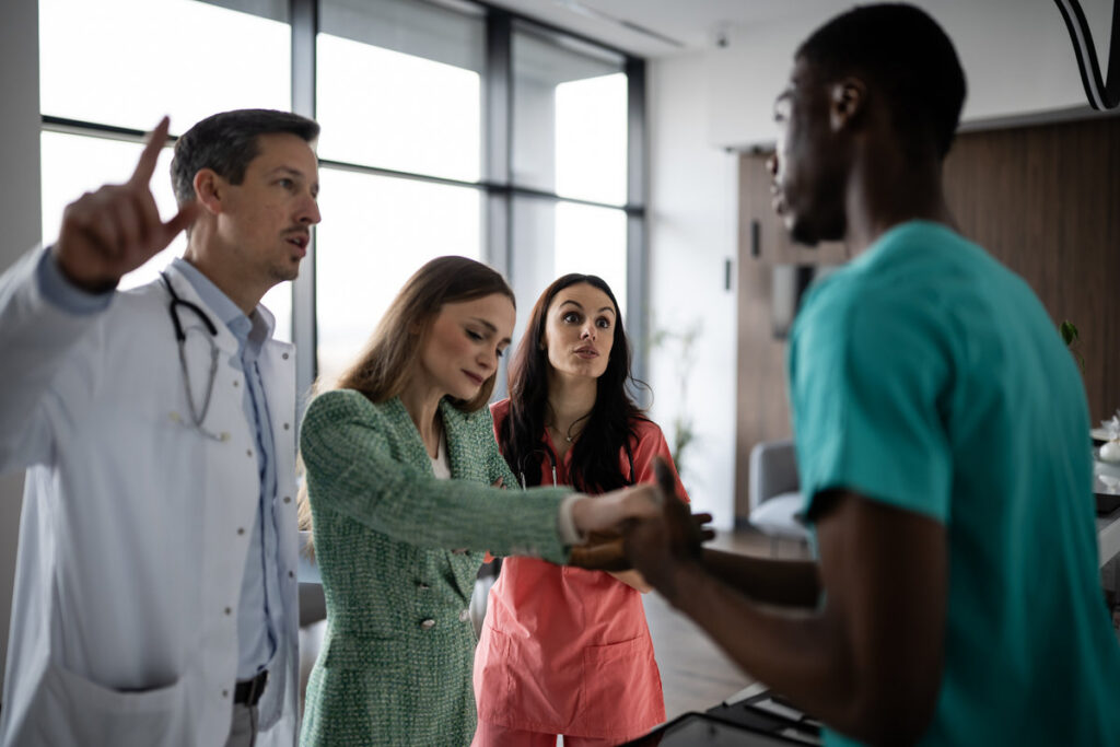 Medical team discussing with doctor pointing finger, showing conflict and disagreement in a modern healthcare environment